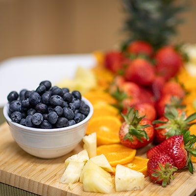 Wooden cutting board with a bowl of blueberries, orange slices, strawberries, and cheese wedges